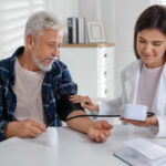 A doctor measures a patient's blood pressure at a table in the hospital during treatment for hypertension management.
