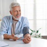 Senior man measuring blood pressure at table indoors.